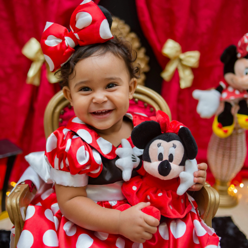 Cute little girl holding a mickey mouse toy and dressed in red and white polka dots
