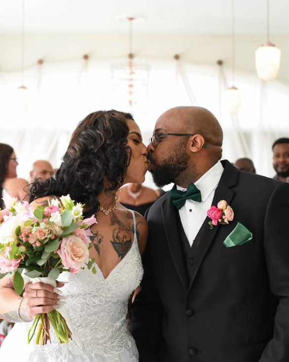 Black bride and groom in white dress and black tux with pink flowers kissing