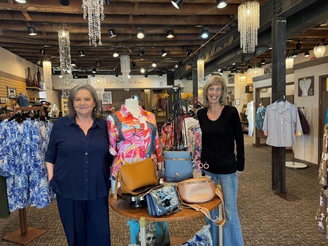 Two middle aged women smiling inside a beautiful boutique with chandeliers