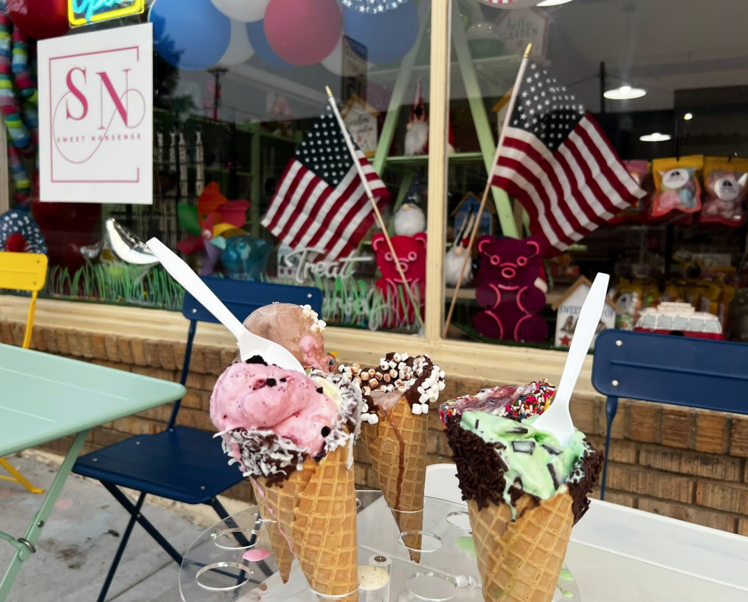 a pink and green ice cream cone in front a a candy storefront